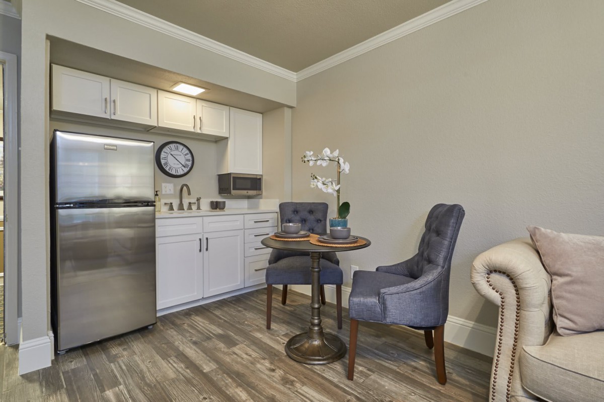 A modern kitchenette with a small dining area featuring two upholstered chairs and a round table.