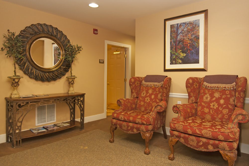 A cozy lobby area with two patterned armchairs, a decorative mirror, and a framed painting.