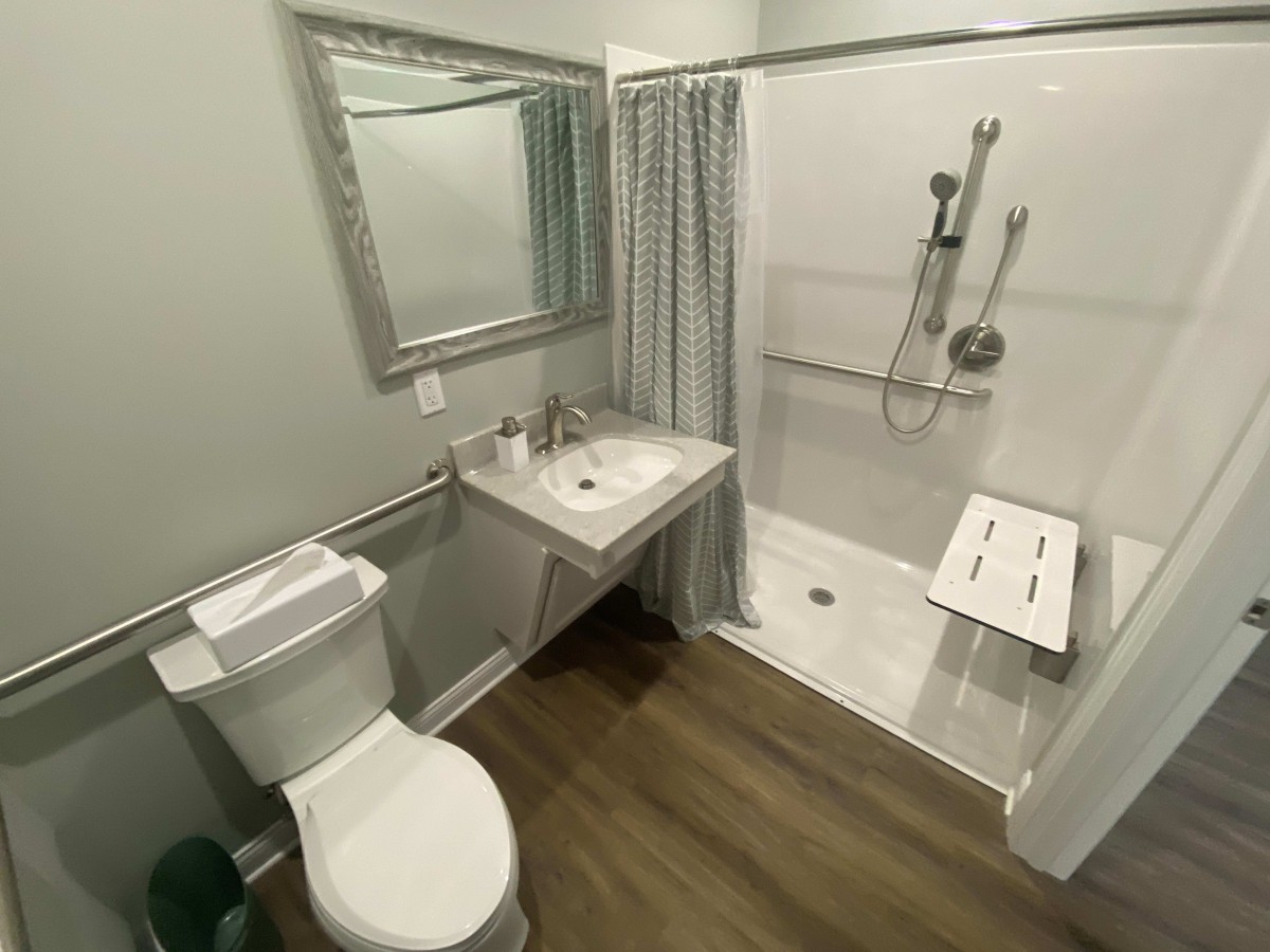 An accessible bathroom with modern amenities, featuring a shower with grab bars and a shower chair.
