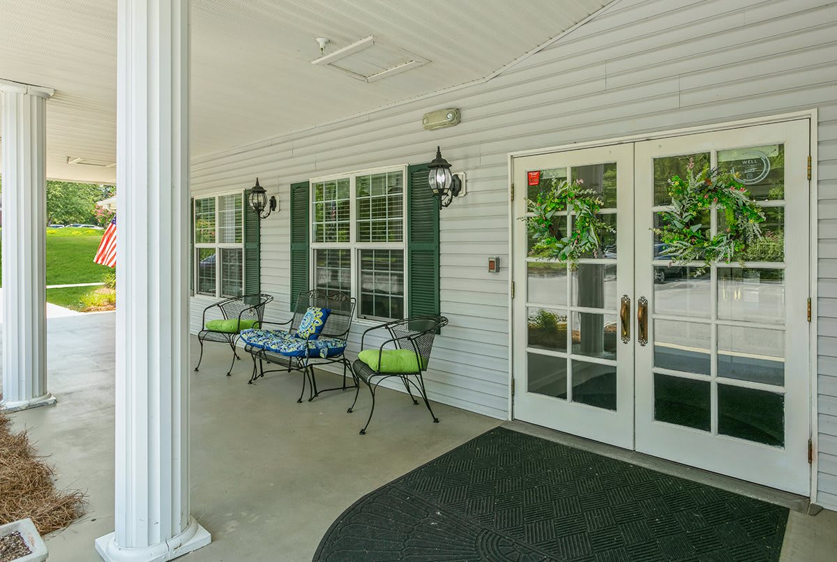 A cozy porch with benches and decorative lanterns next to large windows and double doors.
