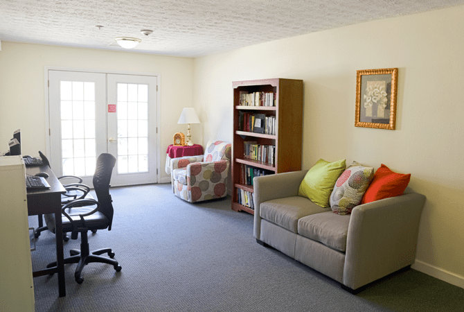 A cozy living room with a sofa, bookshelf, and desk chair.