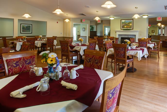 A cozy dining room with neatly set tables, adorned with flowers and surrounded by elegant wooden chairs.