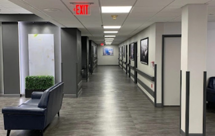 A modern hallway with art on the walls and an exit sign at the ceiling.