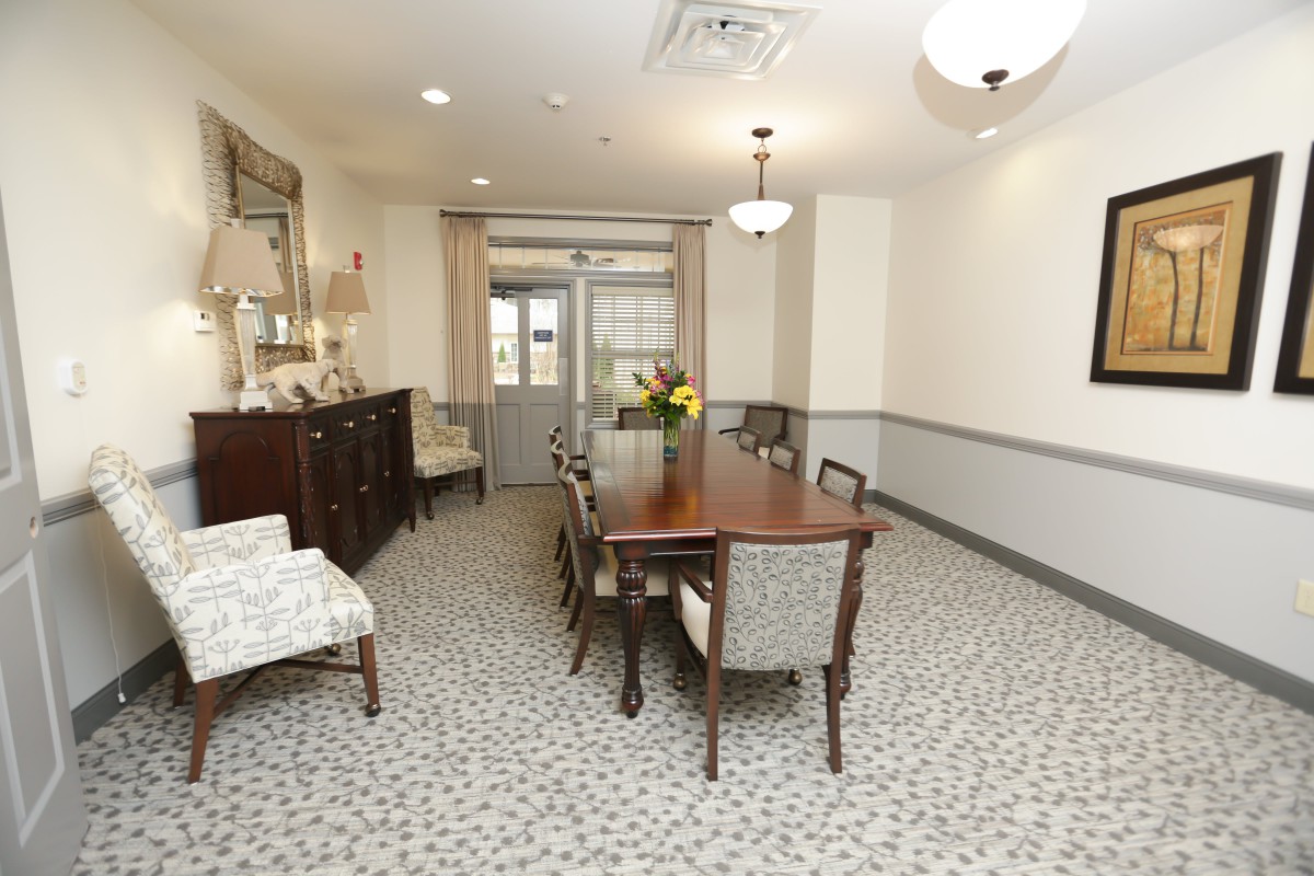 A well-furnished dining room with a wooden table and chairs, decorated with a floral centerpiece, and illuminated by chandeliers.