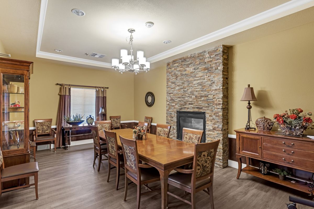 A cozy dining room featuring a large wooden table, a stone fireplace, and elegant lighting.