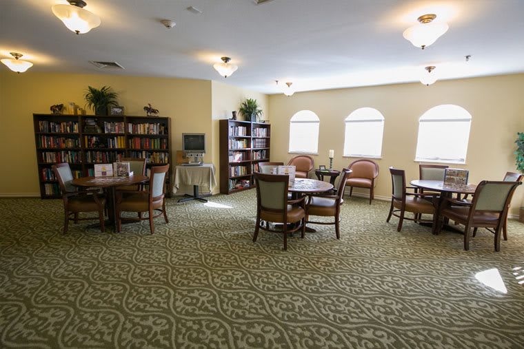 A spacious library with tables, chairs, and bookshelves near windows.