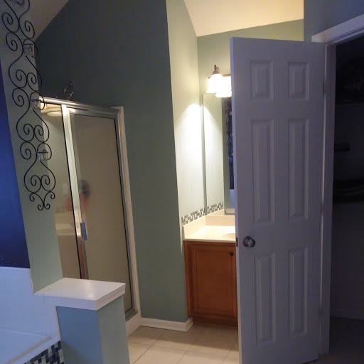 A bathroom with a shower, sink, and mirror, featuring green walls and modern lighting.