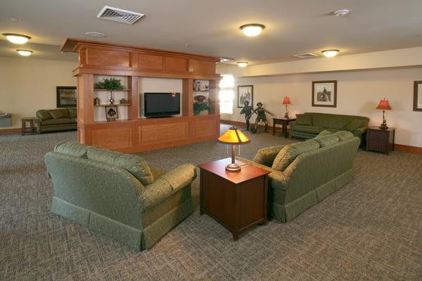 A cozy living room with green sofas facing a television and a wooden coffee table topped with a lamp.