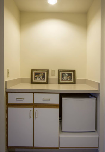 A small kitchenette area featuring framed photographs on a countertop, below which is a set of drawers and a refrigerator.