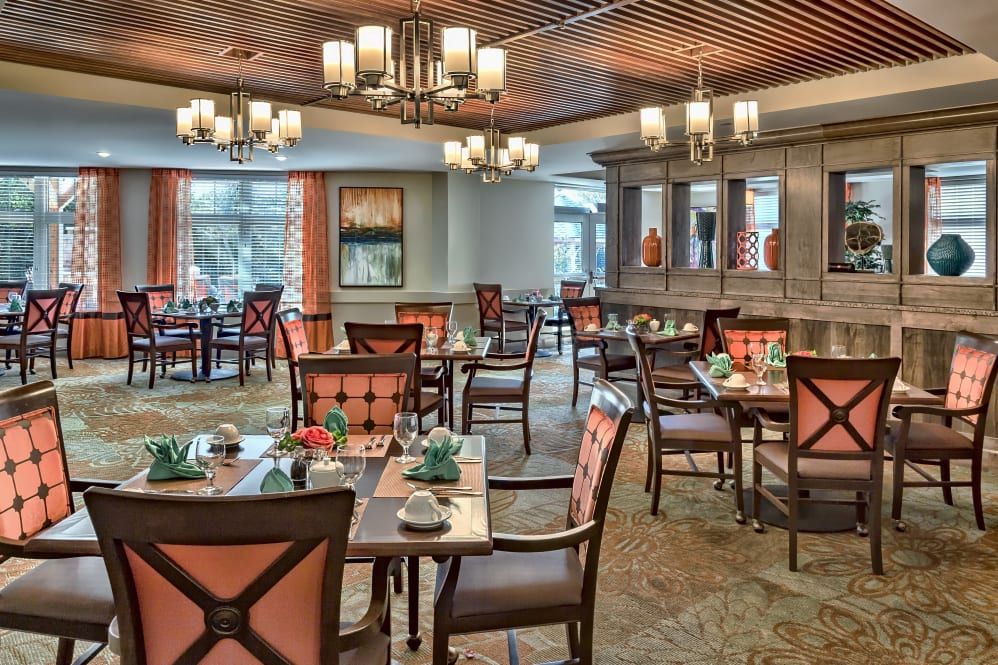 An elegant dining room with neatly arranged tables and chairs, adorned with chandeliers.