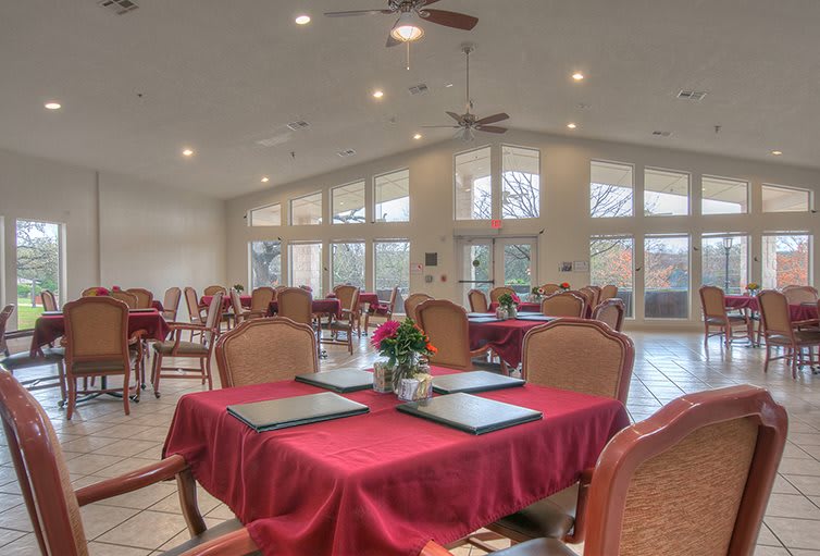 A spacious restaurant dining area with red tablecloths and large windows letting in natural light.