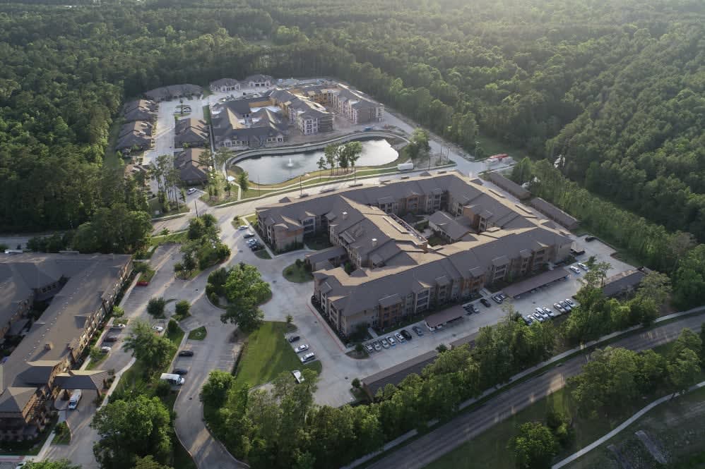An aerial view of a residential complex surrounded by lush greenery and parking areas.