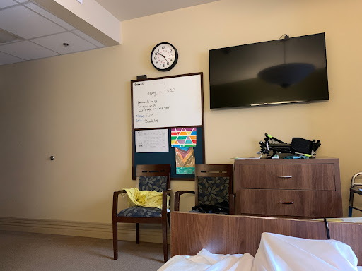 A quiet patient room in a hospital, featuring a clock, television, and comfortable seating area.