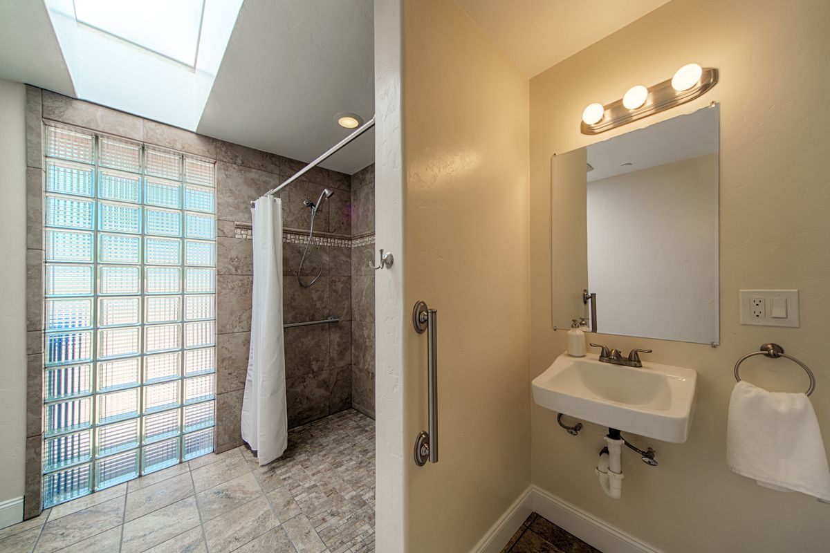 A modern bathroom with a sink, mirror, and shower area separated by a curtain.