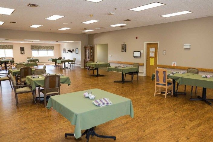 An empty dining hall with neatly arranged tables and chairs covered in green tablecloths.