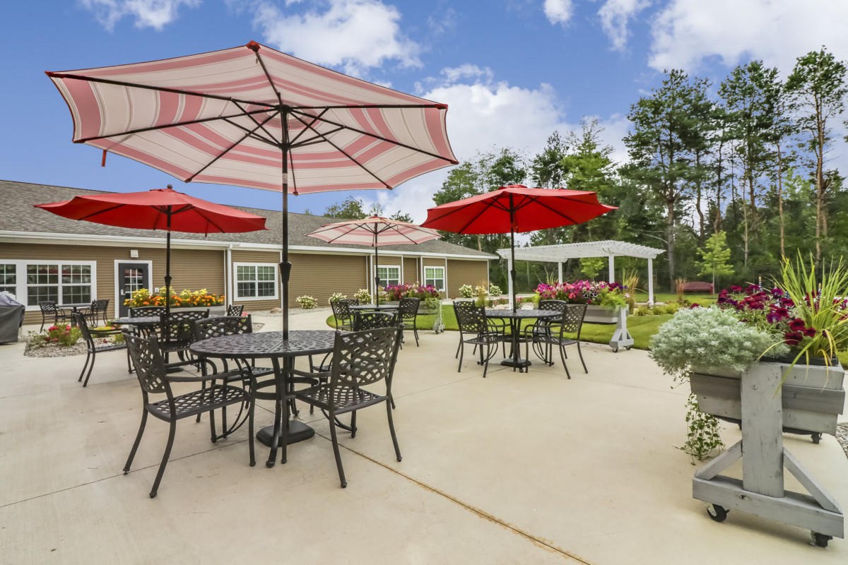 A sunny outdoor patio with tables, chairs, and red umbrellas.