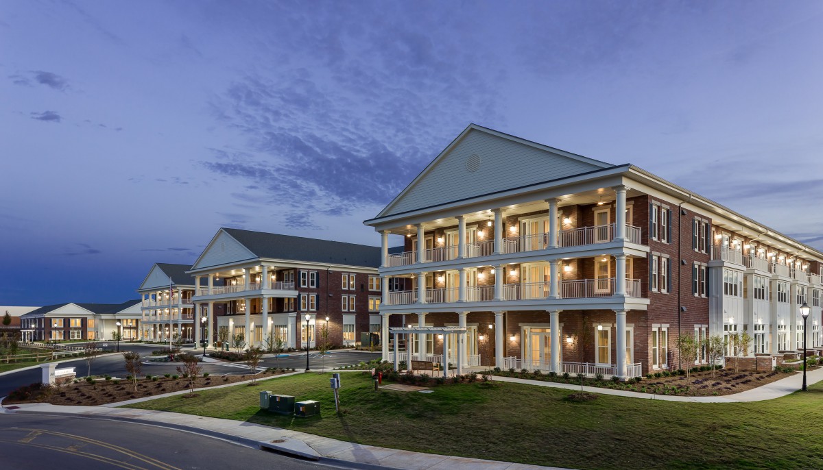 An evening view of a well-lit apartment building with surrounding landscaping.