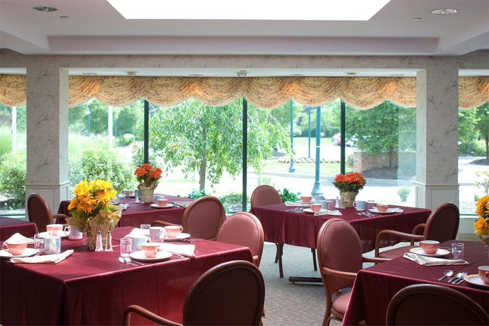 A well-lit restaurant dining area with tables set next to large windows, offering a pleasant view.
