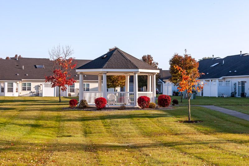 A picturesque gazebo surrounded by autumn trees and a neatly mowed lawn in a suburban area.