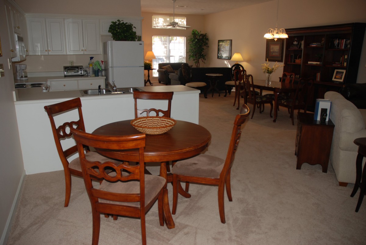 A cozy dining area with a wooden table and chairs, adjacent to a kitchen and living room.