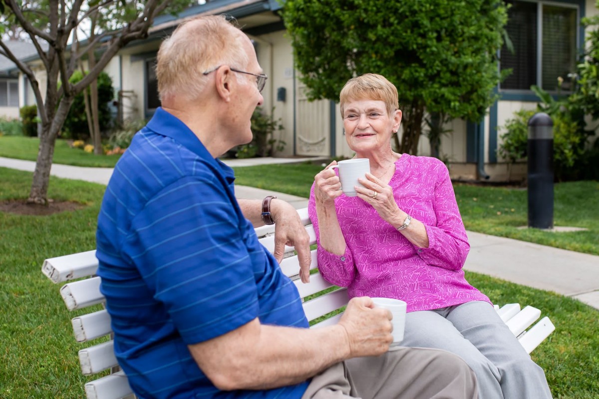 An elderly couple enjoying coffee and conversation on a park bench.