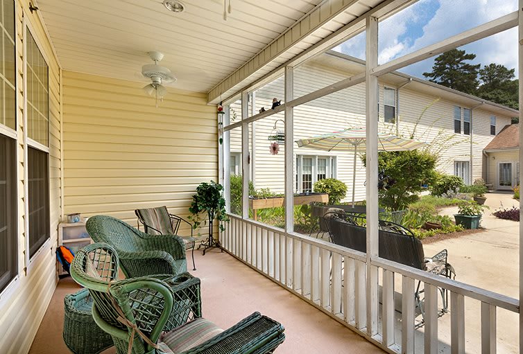 A cozy screened porch with wicker chairs and a garden view, perfect for relaxing.