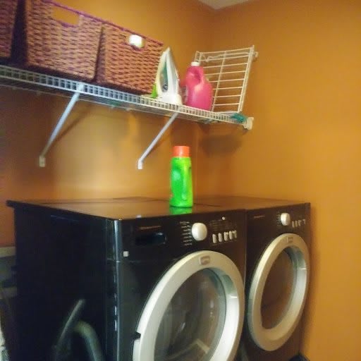 A laundry room featuring a washing machine and dryer, with shelves holding detergent, an iron, and baskets.