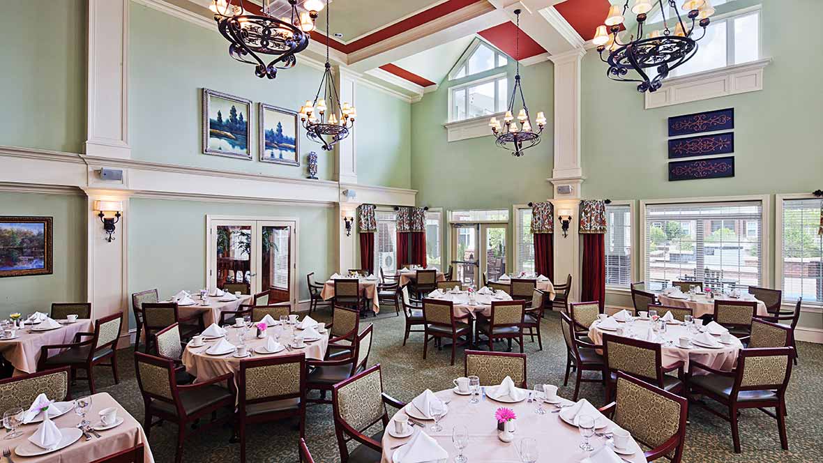 Elegant dining room with high ceilings, chandeliers, and neatly arranged tables.