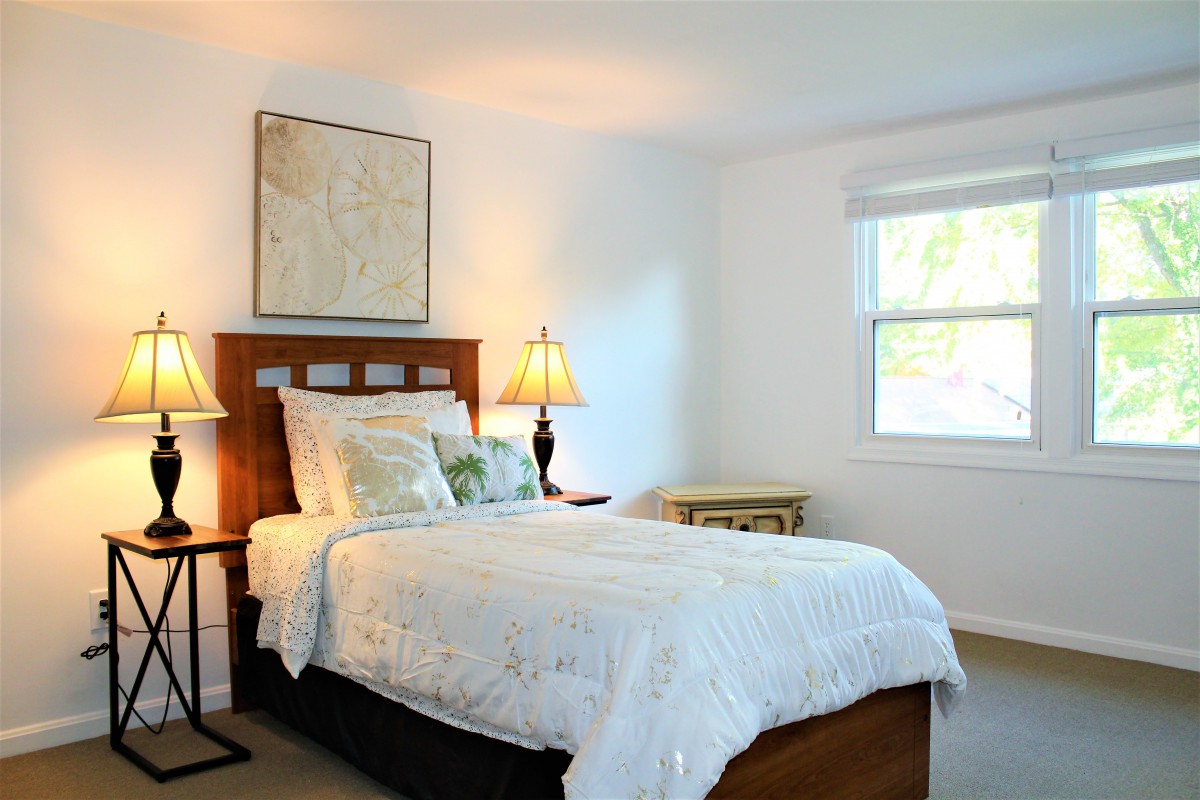 A cozy bedroom with a neatly made bed, decorated with lamps and natural light streaming through the window.