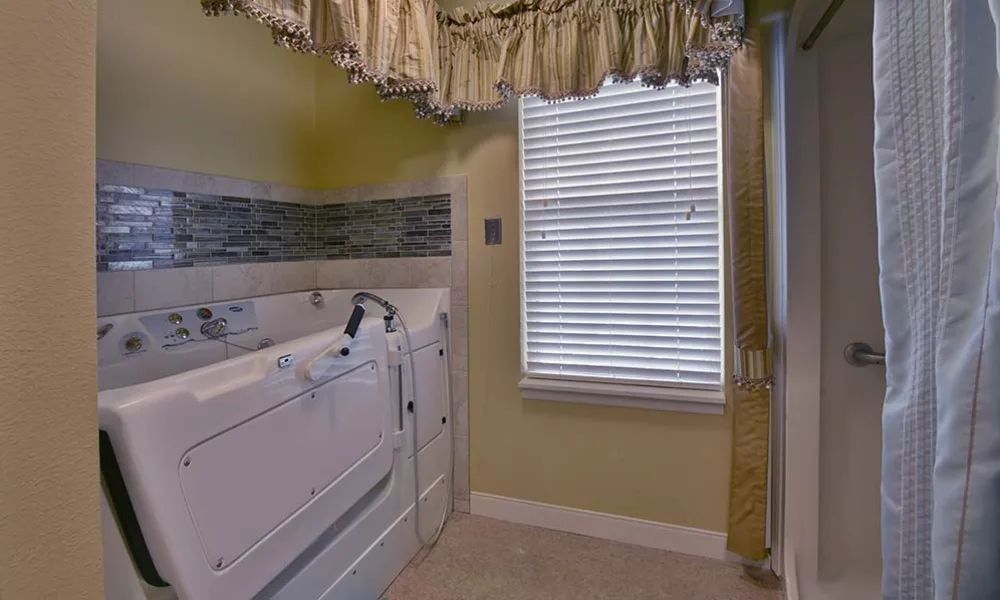 A bathroom with a walk-in bathtub and a window with blinds and curtains.