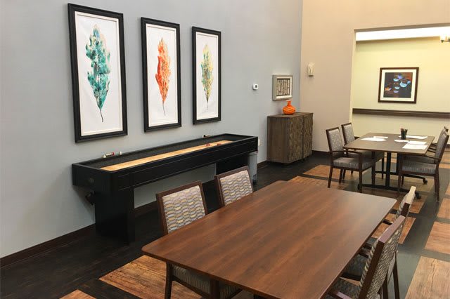 A modern dining room with a wooden table, chairs, and framed leaf artwork on the wall.