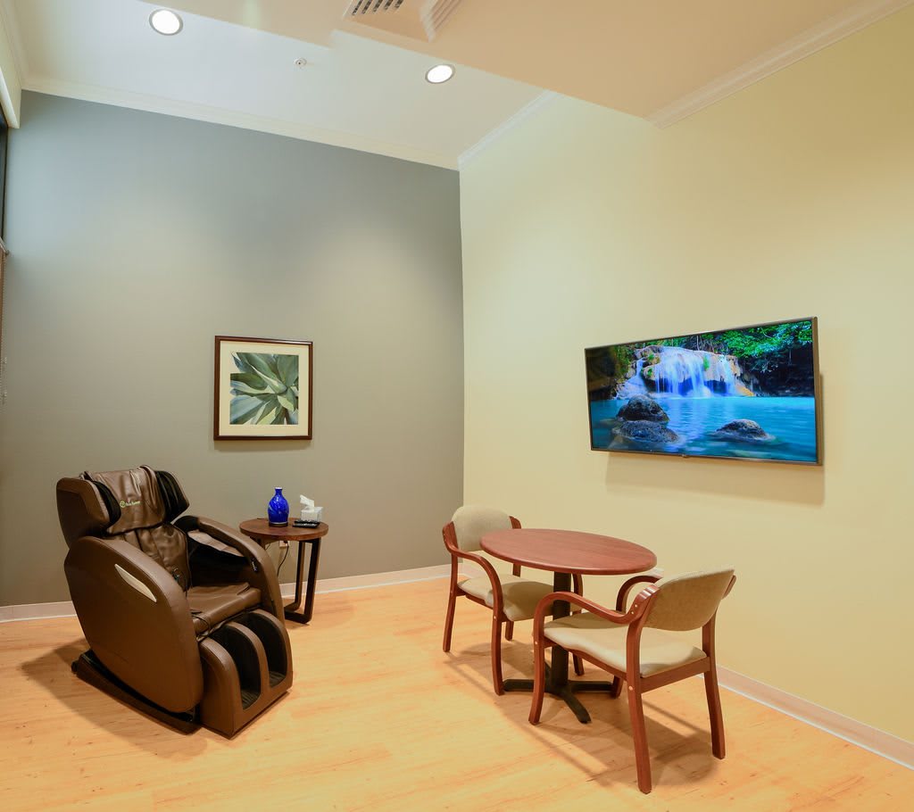 A cozy room featuring a massage chair, a small table with chairs, and a television mounted on the wall.
