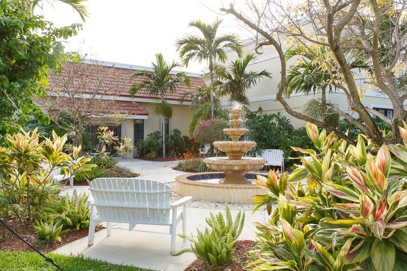 A tranquil garden featuring a tiered fountain surrounded by lush tropical plants and outdoor seating.