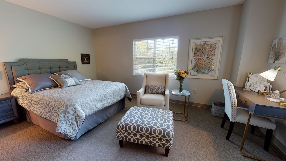 A modern bedroom with stylish decor, featuring a bed, comfortable chair, and patterned ottoman.