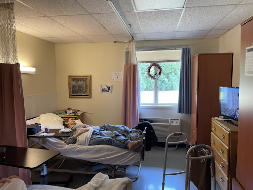 A view of a hospital patient room with two beds and windows letting in natural light.
