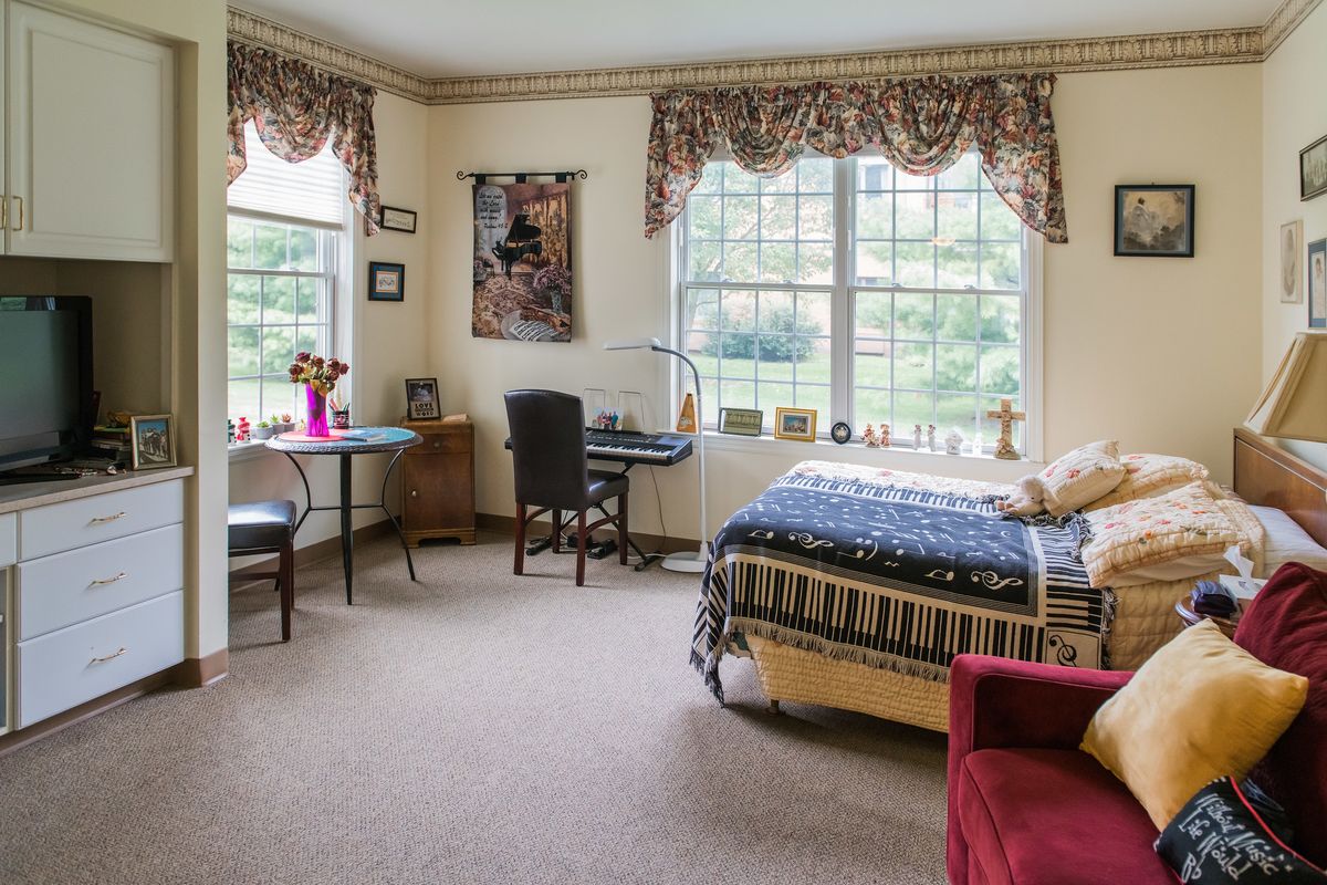 A cozy bedroom with large windows, featuring a bed, desk, and chair.