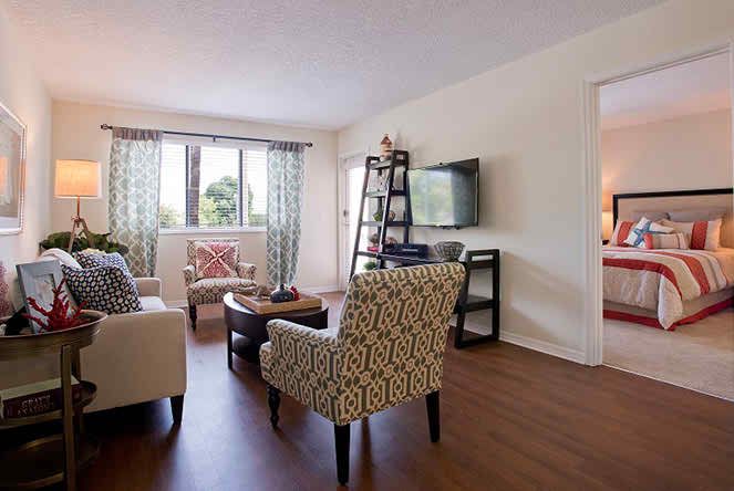 A cozy living room with patterned chairs, a sofa, television, and large windows.
