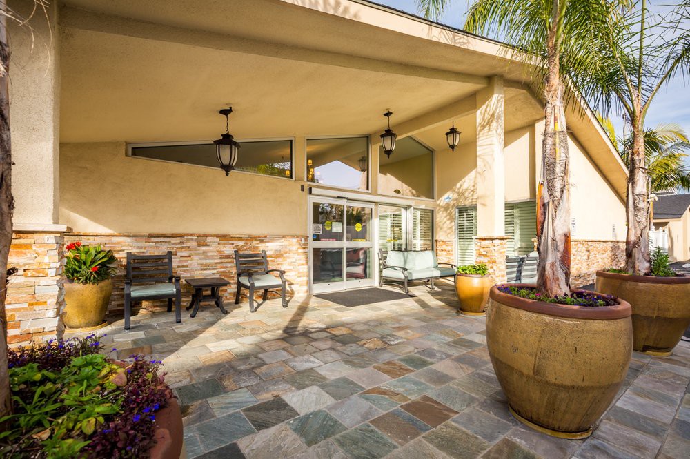 A welcoming building entrance featuring tile flooring, outdoor seating, and large planters.