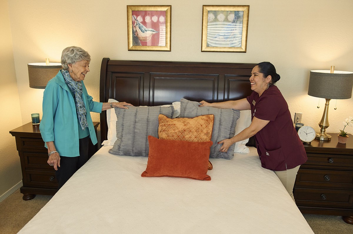 Two people are making a bed together, placing decorative pillows on it in a bedroom setting.
