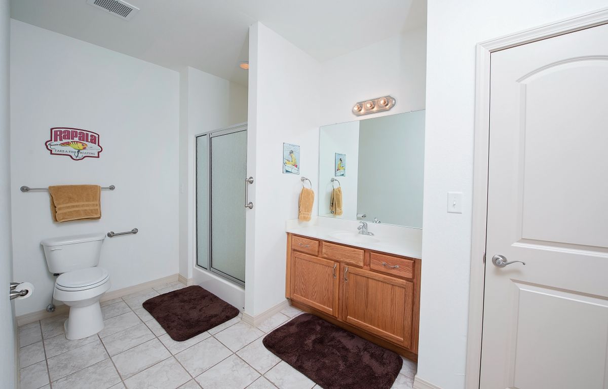 A spacious bathroom with a shower, vanity, and mirror, featuring tile flooring and brown rugs.