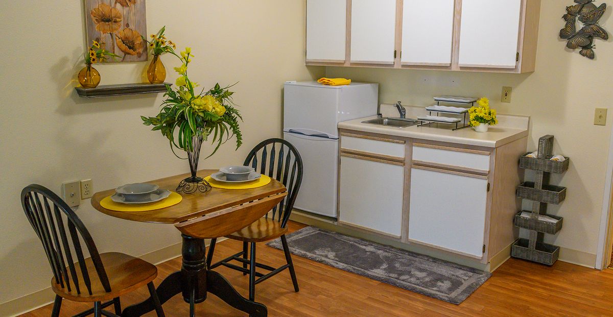 A compact kitchen and dining area featuring a small table set for two, with decorative flowers.
