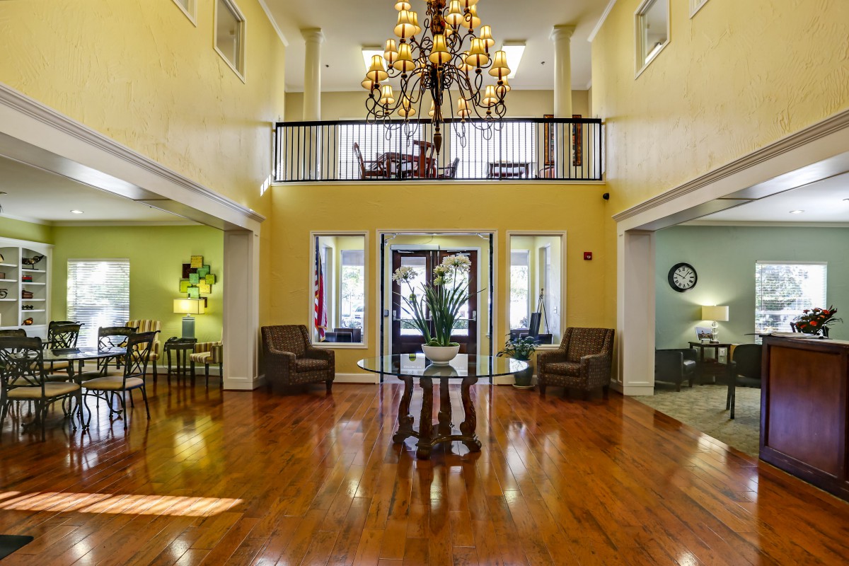 A spacious and elegant foyer with a large chandelier, wooden floors, and comfortable seating.