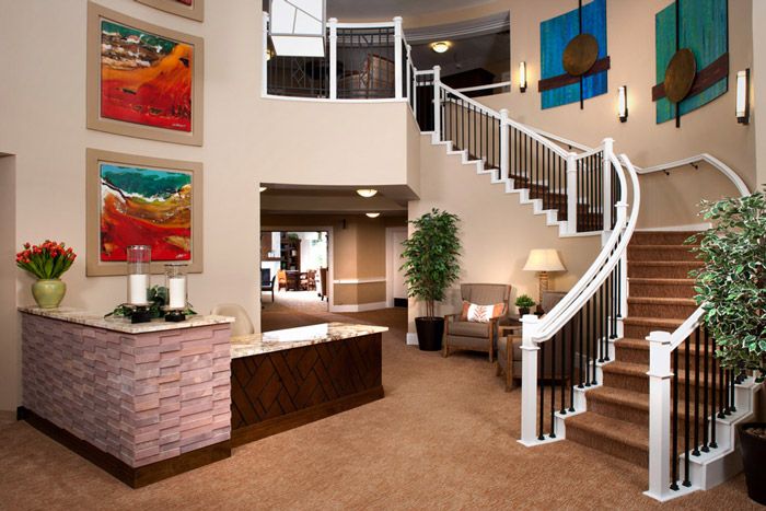 A modern lobby featuring a grand curved staircase, reception desk, comfortable seating, and vibrant artwork on the walls.