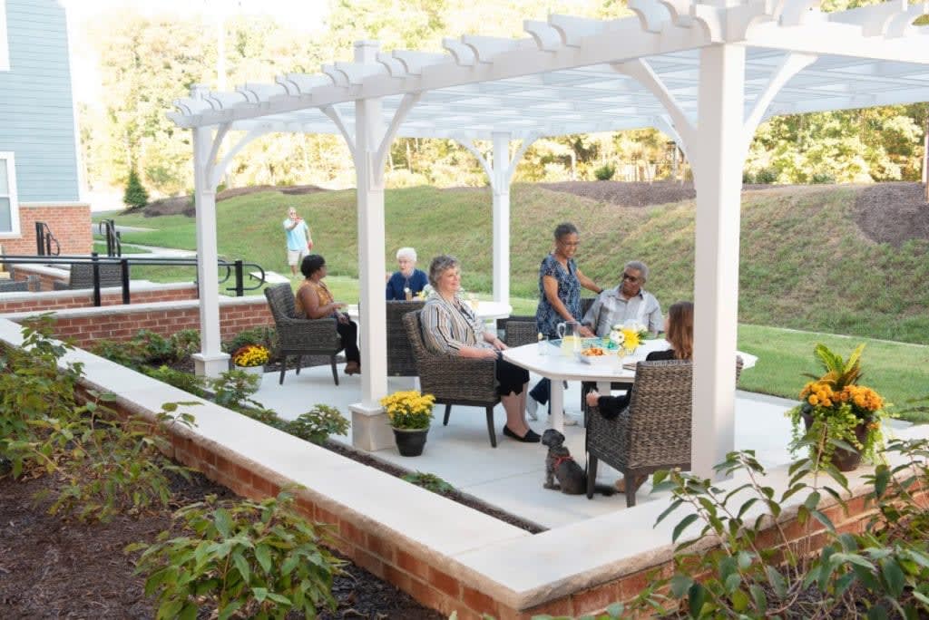 A group of people socializing under a pergola in a garden setting.