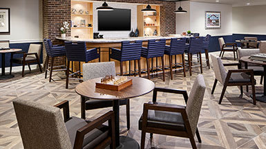 A modern bar area with high chairs, a chess board table in the foreground, and a mounted television with sleek interior design elements.