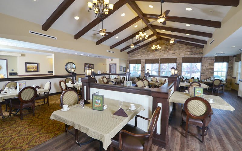 An elegant restaurant interior with neatly arranged tables and chairs, featuring wooden ceiling beams and stylish lighting.