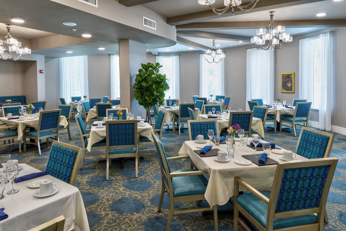 Elegant dining room with neatly set tables and chandeliers overhead.