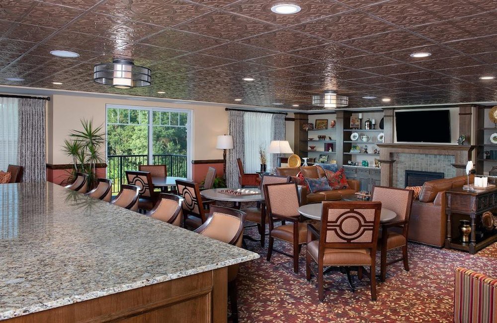 A cozy lounge and dining area featuring upholstered chairs, multiple tables, a bar counter, and detailed ceiling design.
