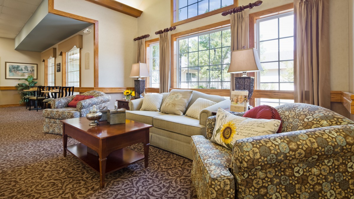 A cozy living room with a sofa and patterned armchairs, illuminated by natural light from large windows.