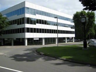 Modern office building with glass windows and a minimalist design surrounded by greenery.